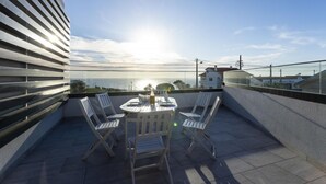 Eine Dachterrasse mit Tisch und Stühlen, mit Blick auf die Küste.