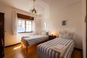 A bedroom with two single beds, a window with curtains, a bedside table with a lamp, and a framed picture on the wall. - Casa do Pedro by Acasadascasas (Mafra)