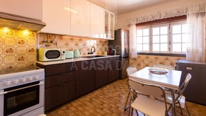 A kitchen with a stove, microwave, and refrigerator. There is a dining table with chairs and a window with curtains.