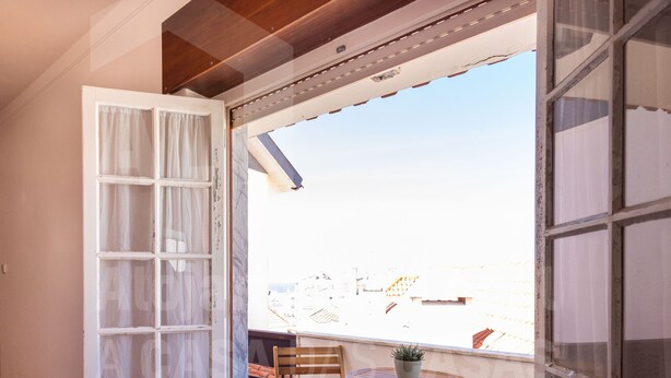 An open door leading to a balcony with a wooden chair, a small table, and a potted plant.