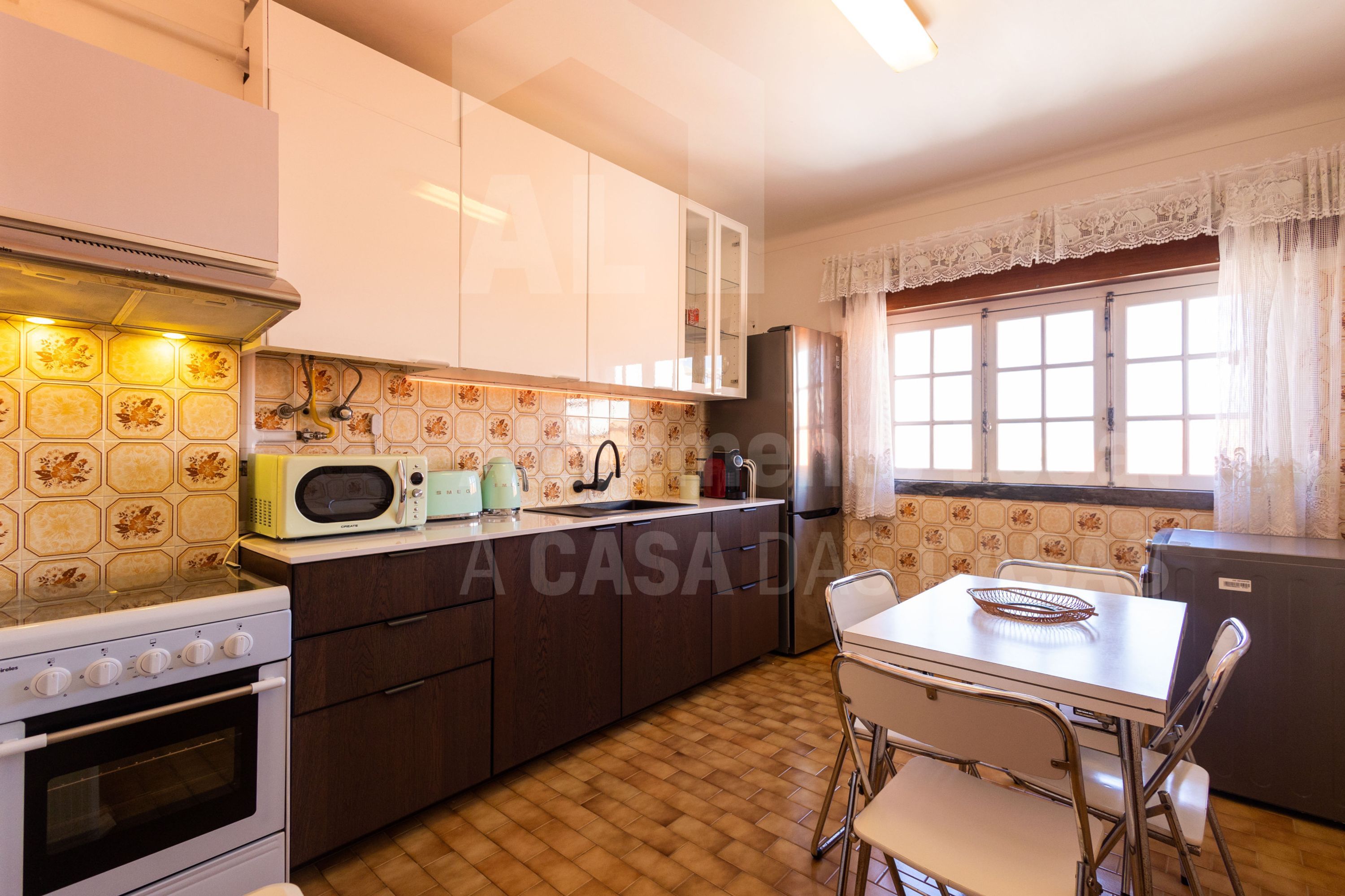 Une cuisine équipée d’une cuisinière, d’un four à micro-ondes et d’un réfrigérateur. On y trouve une table à manger avec des chaises, ainsi qu’une fenêtre avec des rideaux.