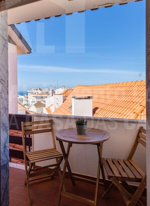 A balcony with two wooden chairs and a small table, overlooking a cityscape with terracotta rooftops. - Casa do Pedro by Acasadascasas (Mafra)