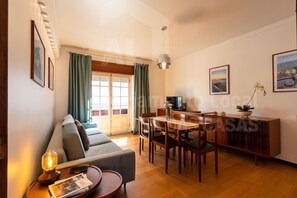 A spacious living area with a sofa, dining table, and chairs. There is a TV, a lamp, and a plant on the table. - Casa do Pedro by Acasadascasas (Mafra)
