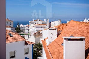 A coastal town with terracotta-roofed buildings, a clear blue sky, and the sea in the background. - Casa do Pedro by Acasadascasas (Mafra)