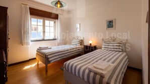 A bedroom with two single beds, a window with curtains, a bedside table with a lamp, and a framed picture on the wall.