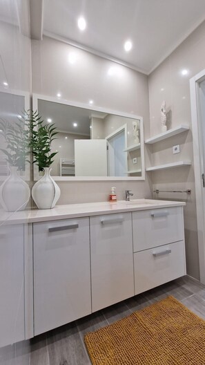 Een moderne badkamer met een witte wastafel, een grote spiegel en een plant.