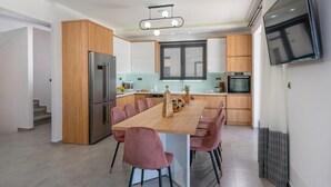 Eine moderne Küche mit einer zentralen Kochinsel, Holzschränken, Edelstahlgeräten und einem an der Wand befestigten Flachbildfernseher.