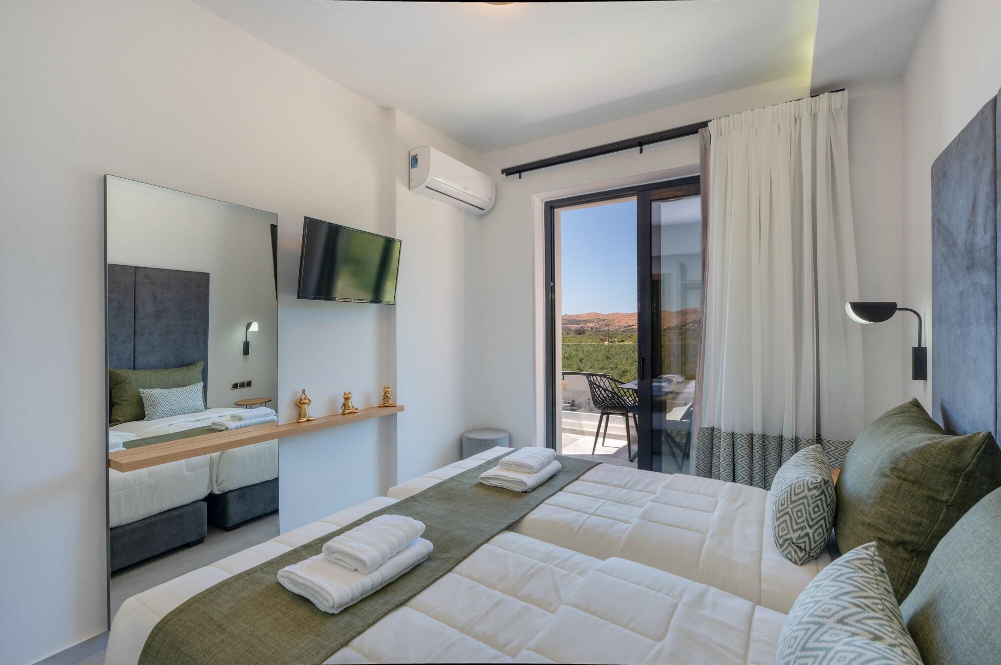 A modern bedroom with a large bed, a TV mounted on the wall, a balcony with a view, and a mounted air conditioner.