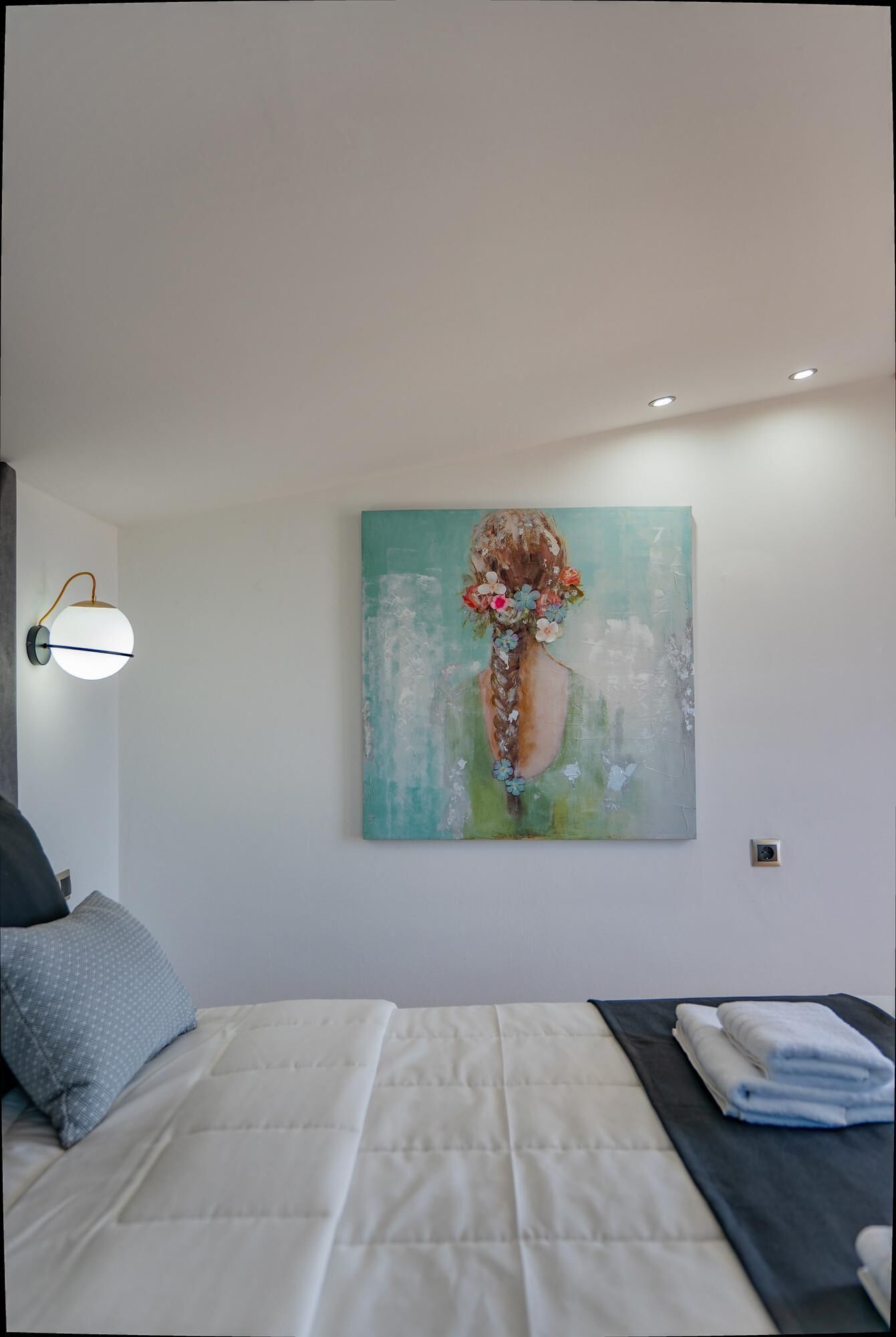 Quarto com cama, pintura na parede, luminária de cabeceira e toalha dobrada no criado-mudo.