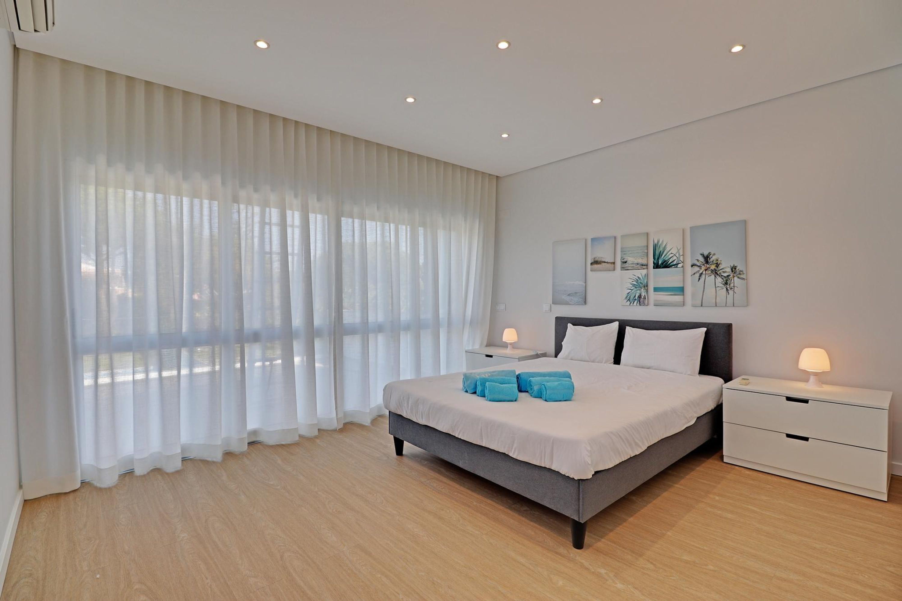 A modern bedroom with a large bed, two bedside tables, and a view of the outdoors through sheer curtains.