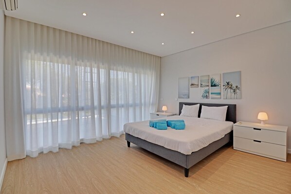 A modern bedroom with a large bed, two bedside tables, and a view of the outdoors through sheer curtains.