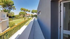 En modern byggnad med en balkong som vetter ut mot en välskött trädgård och de intilliggande husen.