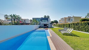 En modern swimmingpool med ett trädäck, omgiven av välskötta häckar och en klarblå himmel.