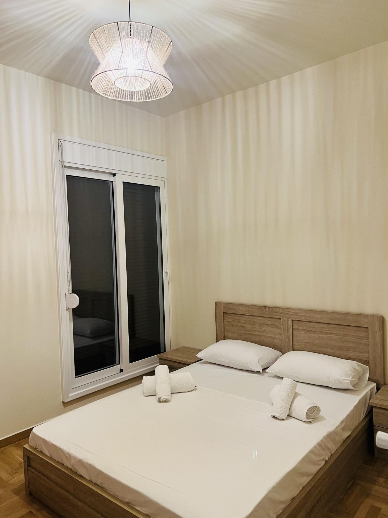 Quarto com uma cama grande, cabeceira de madeira, luminária de teto branca e porta de vidro deslizante.