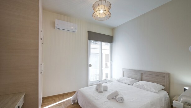 Une chambre moderne avec un grand lit, un luminaire au plafond et une fenêtre équipée de stores.