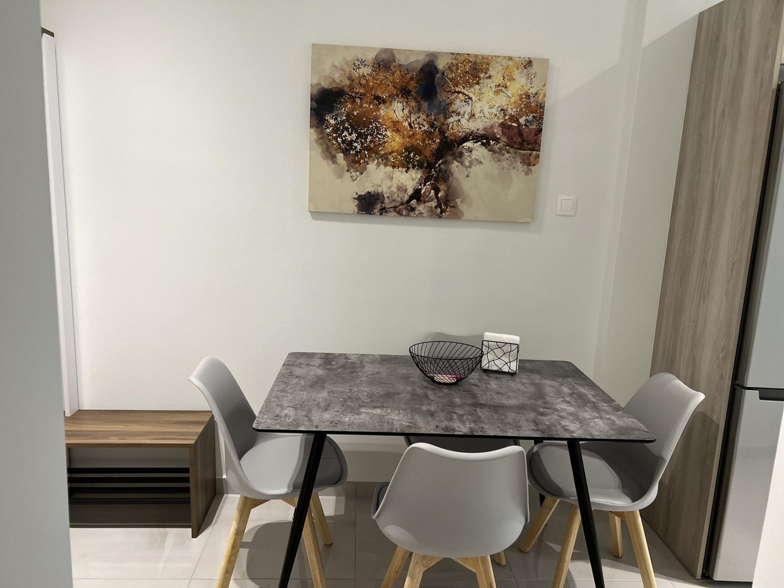 A modern dining area with a grey table, four grey chairs, a black wire basket, and a white tray.