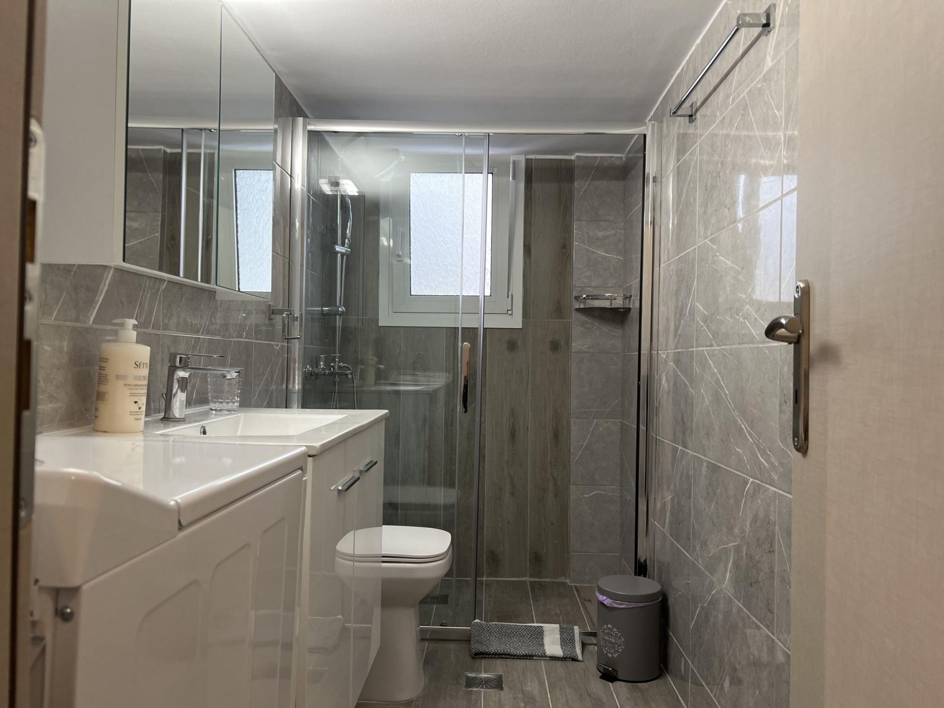 Une salle de bain moderne avec une douche à parois de verre, des toilettes et un lavabo surmonté d’un miroir.