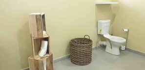 Une salle de bain avec une étagère en bois, un panier en osier et des toilettes.
