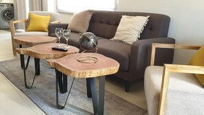 A living room with a sofa, two small wooden tables, a globe, and a washing machine in the background.