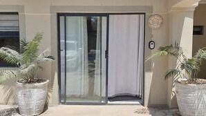 A building entrance with a sliding glass door, potted plants, and a wall-mounted sign.