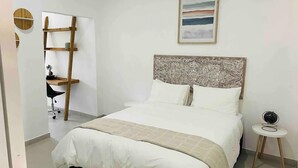 A bedroom with a bed, a bedside table, a chair, a ladder, and a wall-mounted shelf.