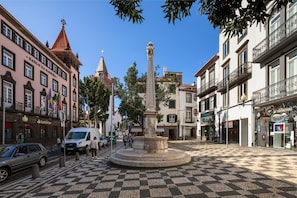 Une place publique avec une fontaine centrale, entourée de bâtiments abritant des commerces.