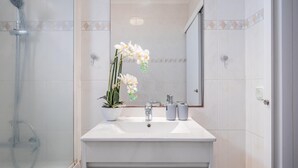 Un baño moderno con tocador blanco, ducha y orquídea en maceta.