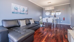Una sala de estar moderna con un sofá de cuero negro, una mesita auxiliar con un jarrón blanco y un cuadro de árboles en la pared.