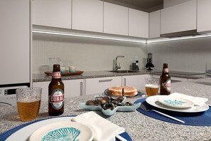 A kitchen with white cabinets, a granite countertop, and a dining area with a plate, a glass, and two bottles of beer.