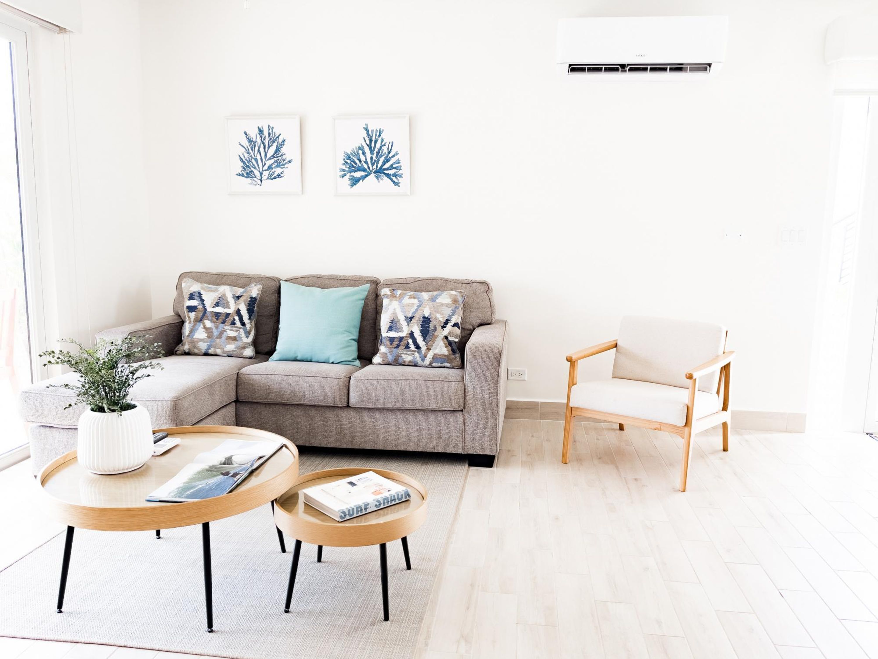 A modern living room with a grey sofa, a wooden coffee table, a white armchair, and two framed artworks on the wall.