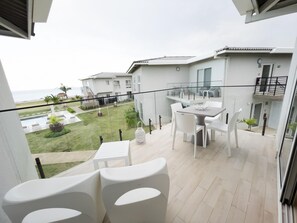 A balcony with white furniture, a glass railing, and a view of a pool and buildings. - Residences C13-1c in Chame (Punta Chame)