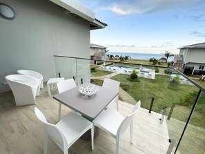 Un balcó amb taula i cadires, amb vista a una piscina i al mar.