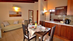 A dining area with a table set for four, a sofa, wooden cabinets, and a kitchen in the background. - Katrina Superior Apartment 5 With Balcony (Rethymno)