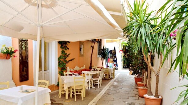 An outdoor café with tables and chairs under umbrellas, surrounded by potted plants and a stone pathway. - Katrina Superior Apartment 5 With Balcony (Rethymno)