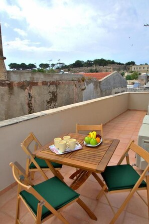 Ein Holztisch mit Stühlen auf einem Balkon, ein Teller Obst und mehrere Tassen.