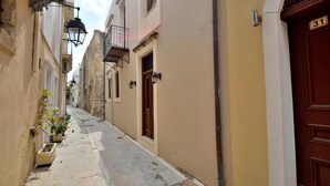 A narrow street with buildings on either side, featuring stone and plaster facades, a wooden door with the number 31, and a small balcony with a metal railing. - Katrina Superior Apartment 5 With Balcony (Rethymno)