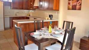 A kitchen with wooden cabinets, a tiled backsplash, and a dining area with a table set for four. - Katrina Superior Apartment 5 With Balcony (Rethymno)
