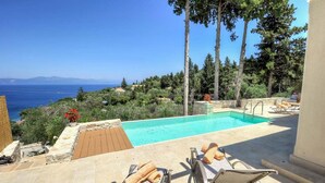 A poolside area with a view of the sea, surrounded by trees and a stone wall. - Apeiron I Villa - Instaworthy Views Ace Location (Paxos)