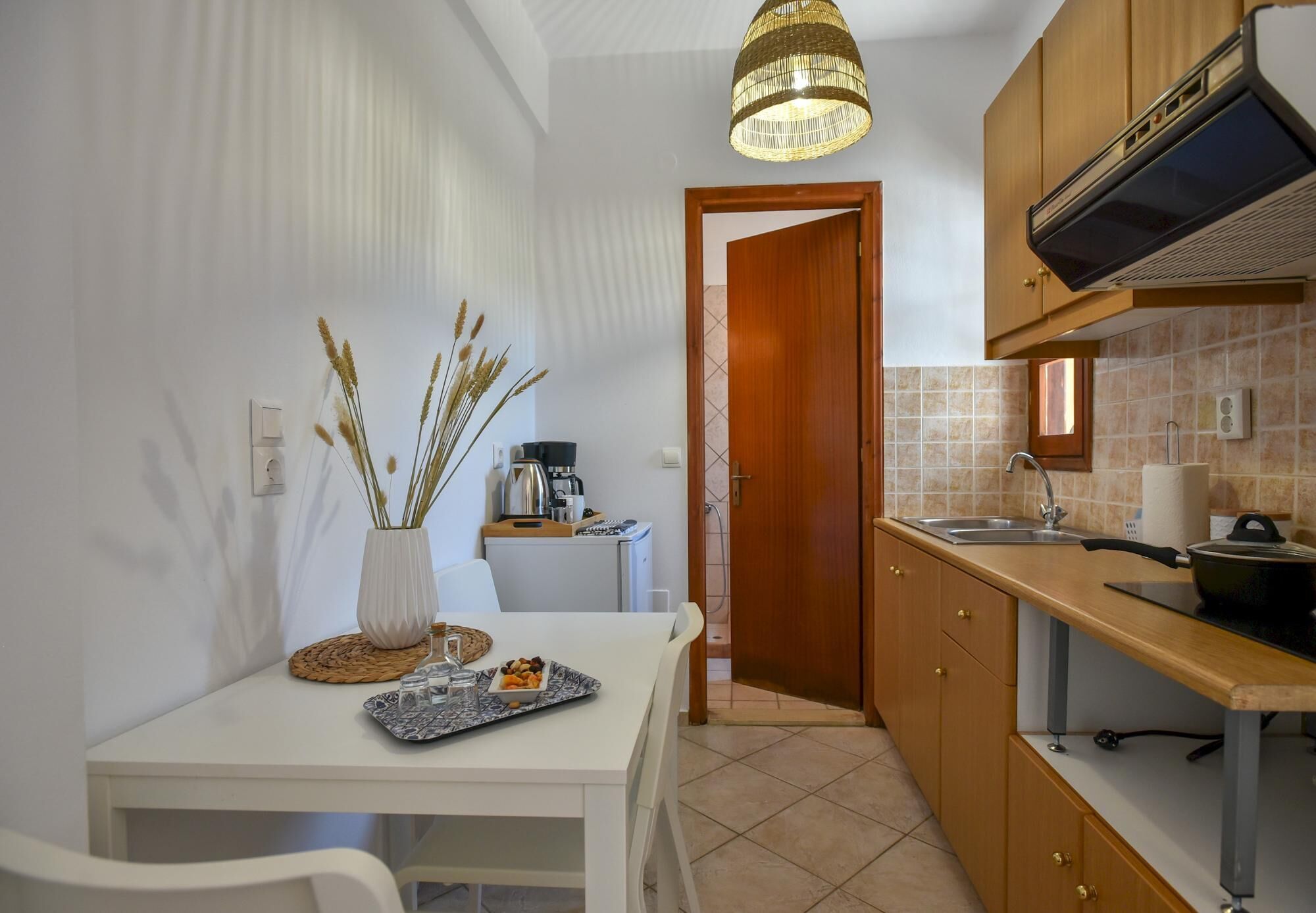 A compact kitchen with a white table, a vase with dried plants, and a small dining area.