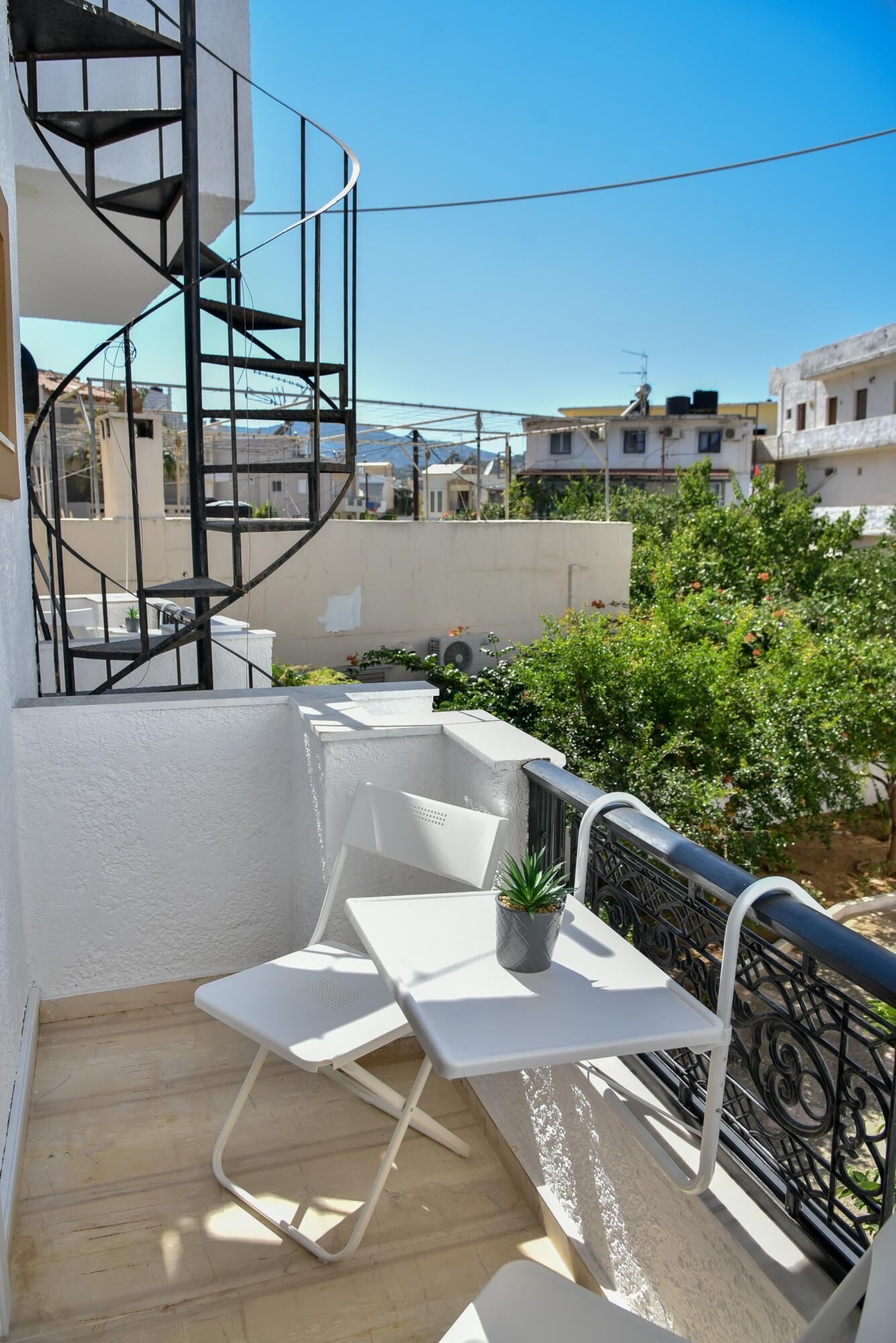 Un balcon avec une table et des chaises blanches, une plante en pot et un escalier en colimaçon.