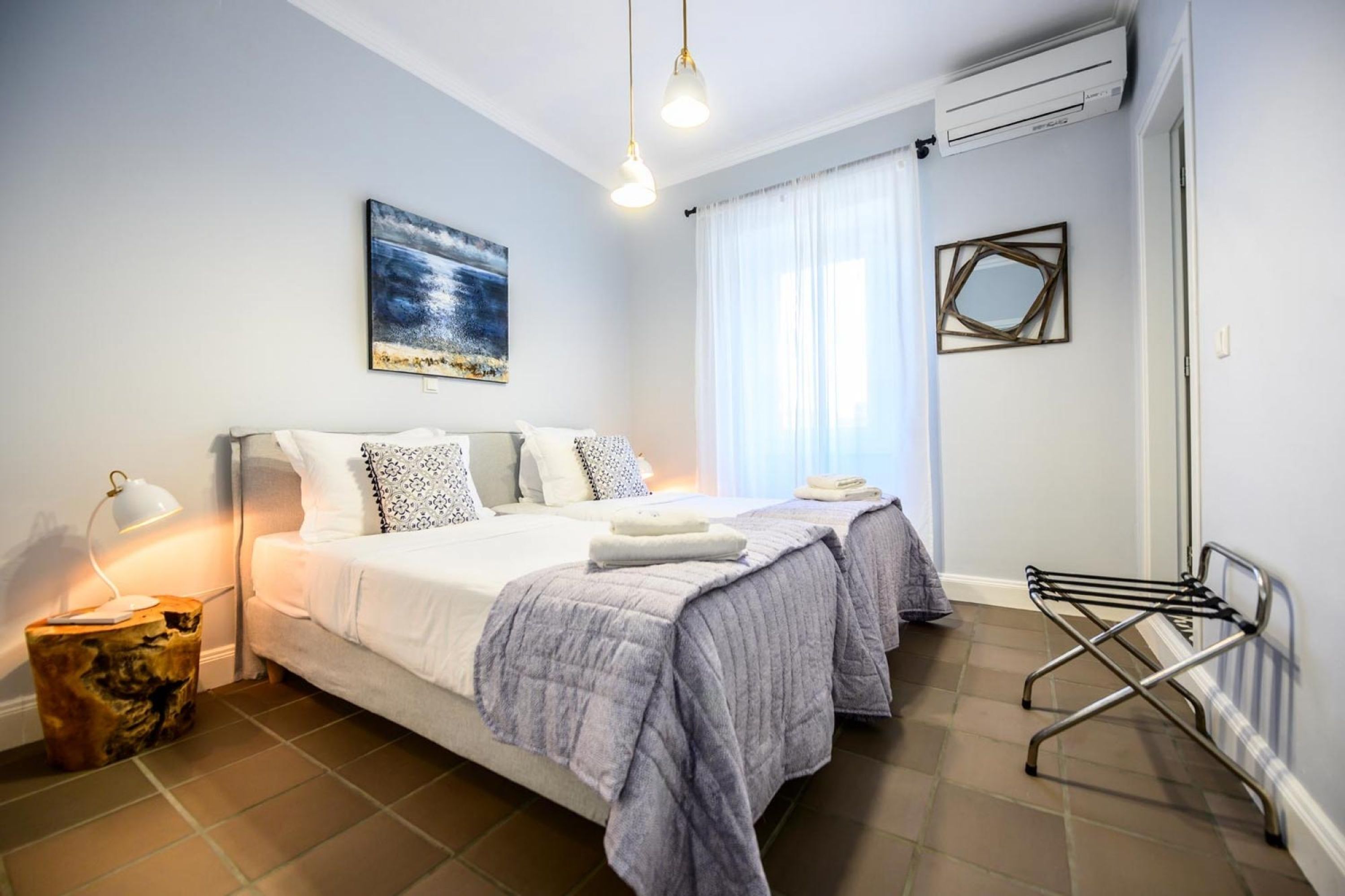A bedroom with two beds, a bedside lamp, a painting, an air conditioner, and a drying rack.