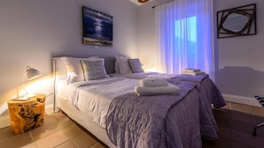 Ein Schlafzimmer mit einem Bett, Nachttischlampen, einem Gemälde und einem Fenster mit Vorhängen.