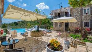 A stone patio with a pool, outdoor seating, and a stone building with a balcony. - Angelina Villa - Four Bedroom Traditional Paxos Villa (Paxos)