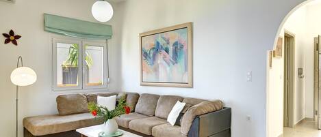 A living room with a sofa, a coffee table, a floor lamp, a painting, and a window with a view of greenery.