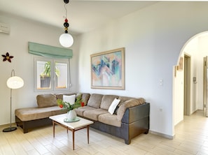 A living room with a sofa, a coffee table, a floor lamp, a painting, and a window with a view of greenery.