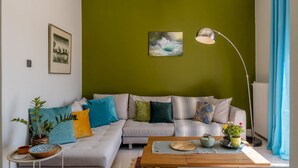 A modern living room with a green accent wall, a grey sofa with colorful cushions, a wooden coffee table, and a floor lamp.