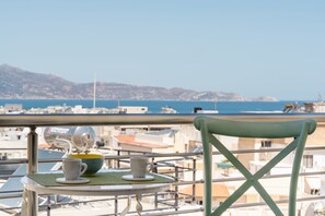 Ein Balkon mit Tisch für zwei Personen, Blick auf eine Küstenstadt mit Bergen im Hintergrund.