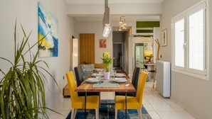 A dining area with a wooden table set for four, yellow chairs, a potted plant, and a painting on the wall.