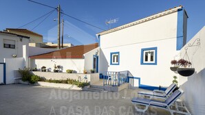 A white building with blue trim, a tiled roof, and a small balcony with a table and chairs. - Casa Aconchego by Acasadascasas (Mafra)