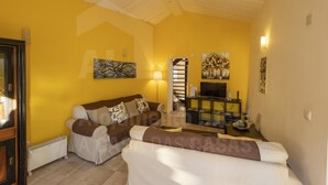 A living room with a yellow wall, a sofa, a TV, and a staircase. - Casa Aconchego by Acasadascasas (Mafra)
